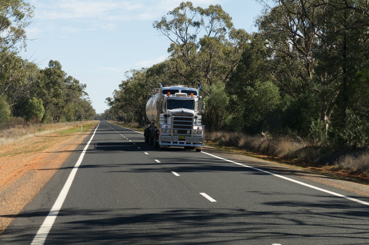 A large truck drives along a scenic rural highway surrounded by trees on a clear day.